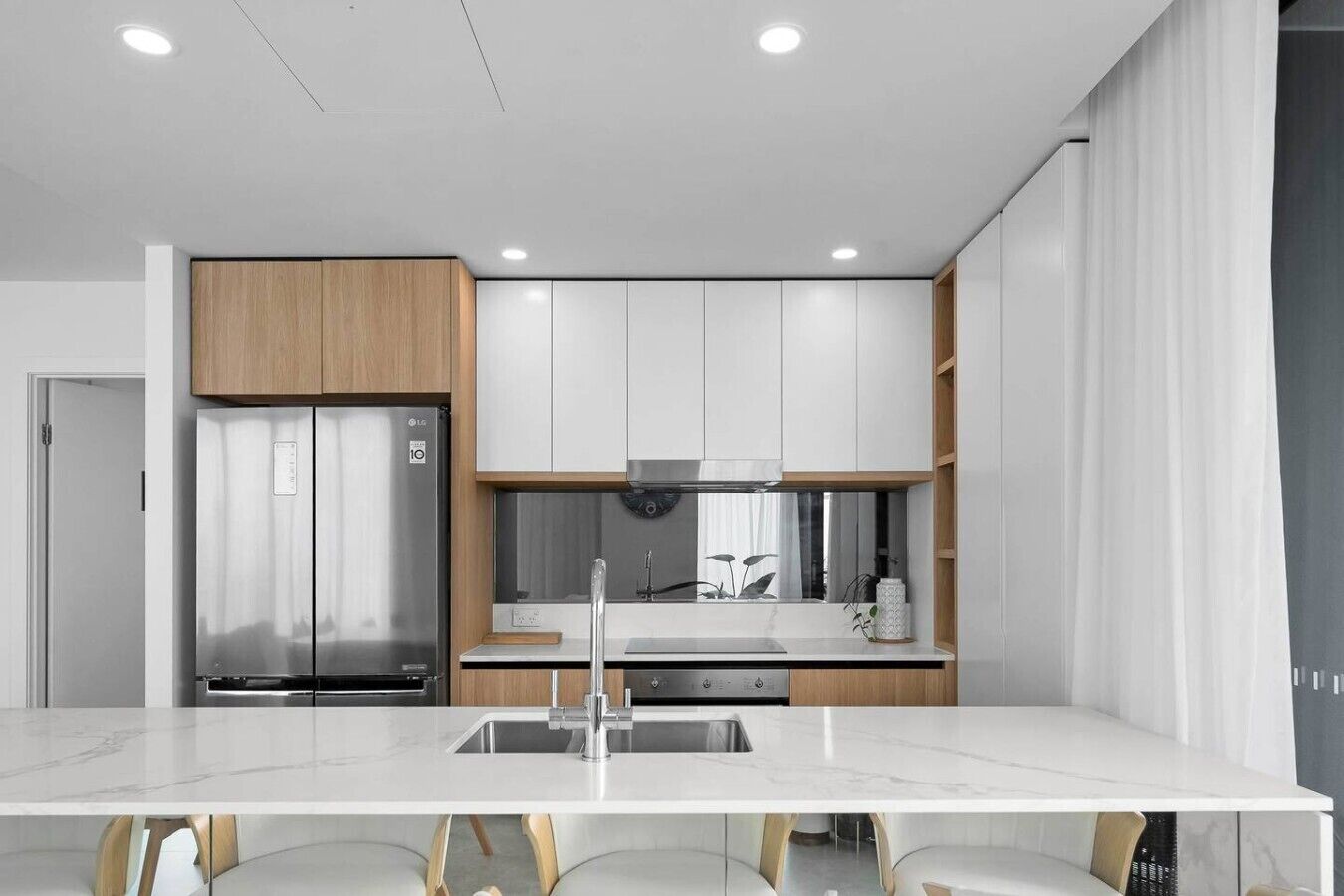 A modern kitchen with a stainless steel refrigerator, white cabinets, and a marble countertop.