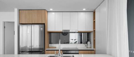 A modern kitchen with a stainless steel refrigerator, white cabinets, and a marble countertop.