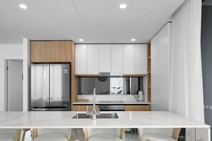 A modern kitchen with a stainless steel refrigerator, white cabinets, and a marble countertop. - 10th Floor Luxury Three Bedroom Beach View Apartment (Broadbeach)