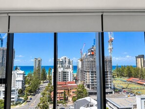 A view from a window overlooking a coastal cityscape with buildings, a clear blue sky, and the ocean. - 10th Floor Luxury Three Bedroom Beach View Apartment (Broadbeach)