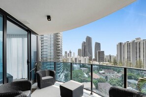 A balcony with wicker furniture, a glass door, and a cityscape view. - 10th Floor Luxury Three Bedroom Beach View Apartment (Broadbeach)
