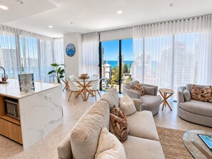 A modern living room with a sofa set, a dining area with a table and chairs, and a kitchen area with a marble countertop. - 10th Floor Luxury Three Bedroom Beach View Apartment (Broadbeach)