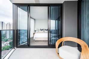 A modern bedroom with a large sliding glass door leading to a balcony, a bed with white linens, and a wooden chair. - Lv 12 Luxury 3 Bedroom APT Hinterland Views (Broadbeach)