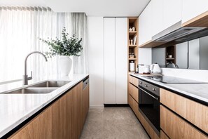 A modern kitchen with a built-in oven, a sink, and wooden cabinets. - Lv 12 Luxury 3 Bedroom APT Hinterland Views (Broadbeach)