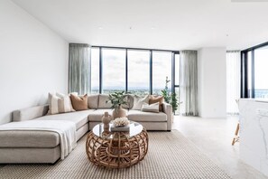 Ein modernes Wohnzimmer mit einem Ecksofa, einem Glastisch und großen Fenstern mit Blick auf die Stadt.