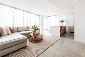 A modern living room with a sofa, a round coffee table, and a kitchen area in the background. - Lv 12 Luxury 3 Bedroom APT Hinterland Views (Broadbeach)
