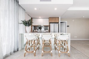 A modern kitchen with white cabinets, a stainless steel refrigerator, and a large island with bar stools. - Lv 12 Luxury 3 Bedroom APT Hinterland Views (Broadbeach)