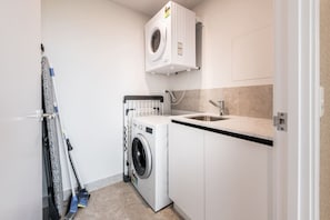 A compact laundry room with a washing machine, a sink, and a drying rack. - Lv 12 Luxury 3 Bedroom APT Hinterland Views (Broadbeach)