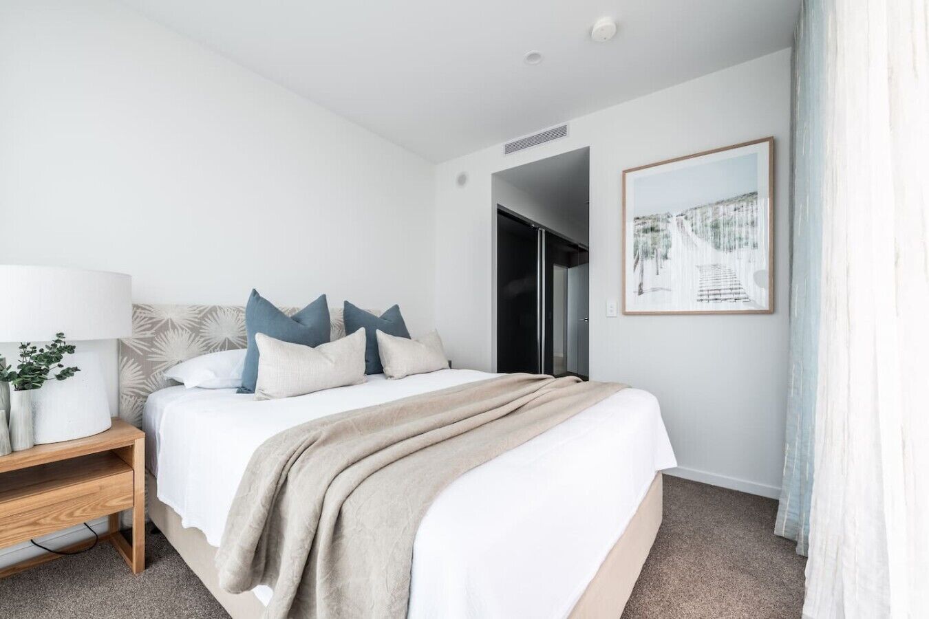 Een hotelkamer met een bed, nachtkastje, lamp en een ingelijst schilderij aan de muur.