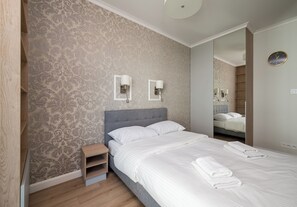 Ein Hotelzimmer mit einem Bett, einem Nachttisch, einem Spiegel und einer Wand mit ornamentalem Wandpapier.