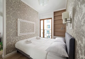A neatly made bed with white linens and pillows, a framed picture on the wall, and a view of the outside through a window. - Pawia Studio Centrum 75 (Warszawa)