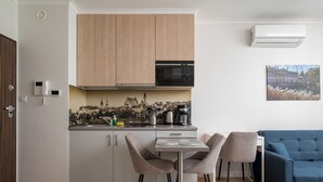 Eine moderne Küche mit Holzschränken, einer Mikrowelle und einer Kaffeemaschine. Im Wohnbereich befindet sich ein Esstisch mit Stühlen und ein blaues Sofa.