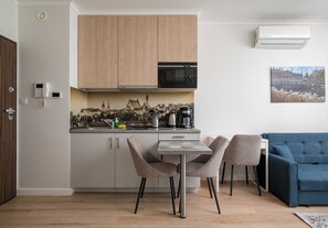 Eine moderne Küche mit Holzschränken, einer Mikrowelle und einer Kaffeemaschine. Im Wohnbereich befindet sich ein Esstisch mit Stühlen und ein blaues Sofa.