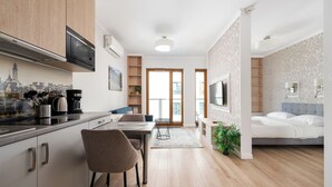 Eine moderne Küche mit Essbereich, ein Wohnzimmer mit Bett und Blick auf die Stadt durch die Fenster.