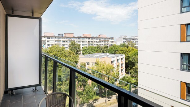 Ein Balkon mit Blick auf eine Wohngegend, darunter eine Reihe von Mehrfamilienhäusern und Bäume.