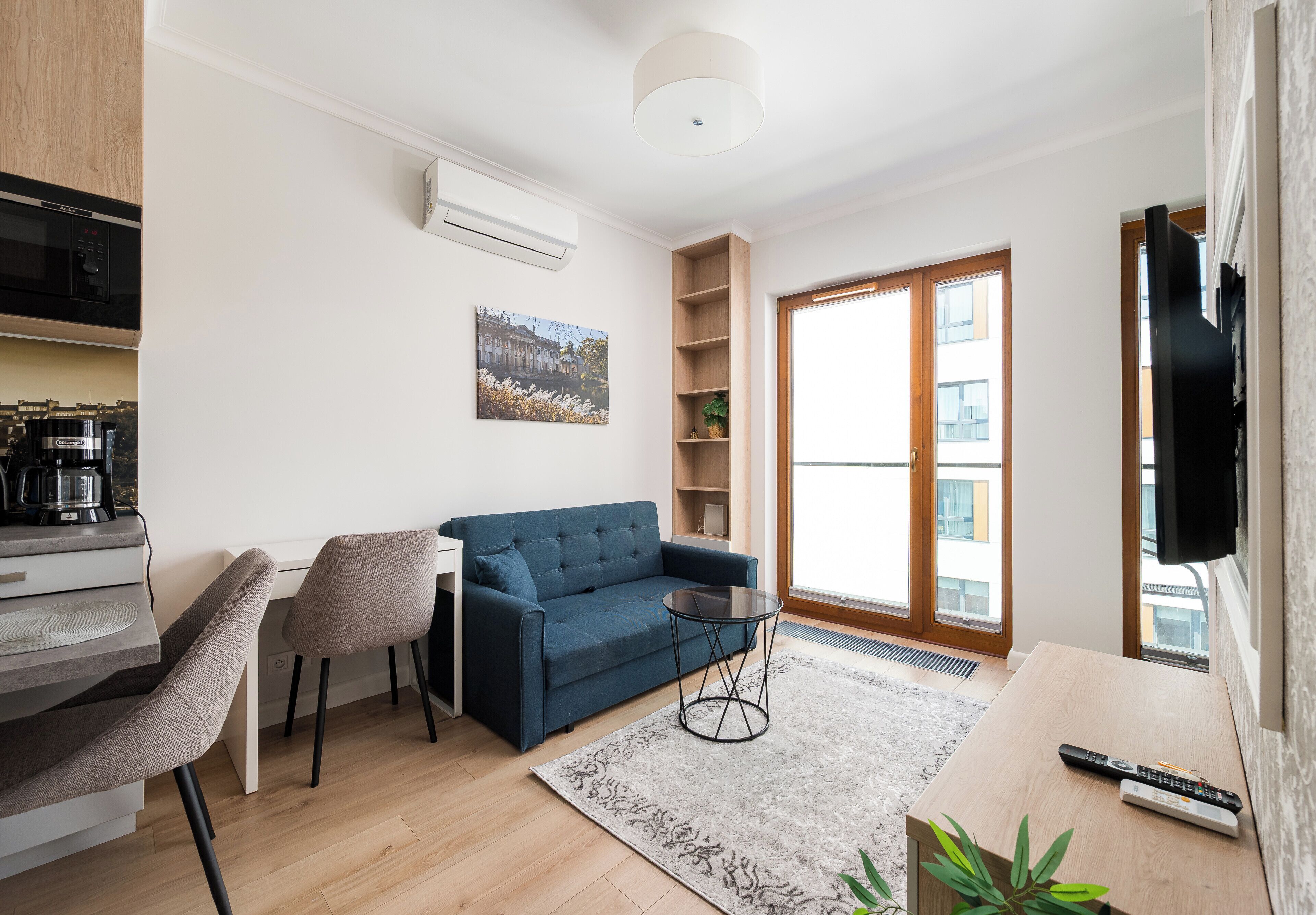 Una sala de estar moderna con un sofá, una máquina de café, un televisor y un ventanal grande.