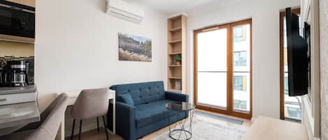 Una sala de estar moderna con un sofá, una máquina de café, un televisor y un ventanal grande.