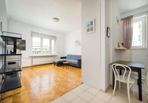 A modern living space with a sofa, a dining table, and a chair. There is a radiator under the windows and a shelf with items on it. - Elektrownia Powiśle Homely Apartment (Warszawa)