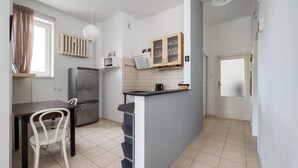 Une cuisine compacte comprenant un réfrigérateur, une table à manger avec des chaises, un petit îlot avec un évier et une fenêtre avec des rideaux.
