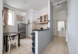 A compact kitchen with a refrigerator, a dining table with chairs, a small island with a sink, and a window with curtains. - Elektrownia Powiśle Homely Apartment (Warszawa)