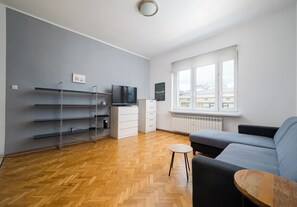 A modern living room with a sofa, a small table, and a TV. There are shelves and a radiator near the window. - Elektrownia Powiśle Homely Apartment (Warszawa)
