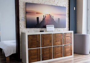 Un salon moderne doté d’un grand téléviseur à écran plat fixé sur un mur à texture, d’un meuble blanc avec des panneaux en bois, d’un canapé gris et d’un plancher en bois.