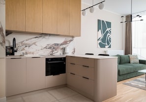 Eine moderne Küche mit eingebautem Geschirrspüler, einer Marmor-Spritzschutzwand und einem grünen Sofa im angrenzenden Wohnbereich.