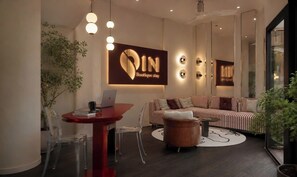 Ein moderner Lounge-Bereich mit einer Couch, einem runden Holzschemel, einem roten Tisch mit einem Laptop und einem an der Wand befestigten Schild.
