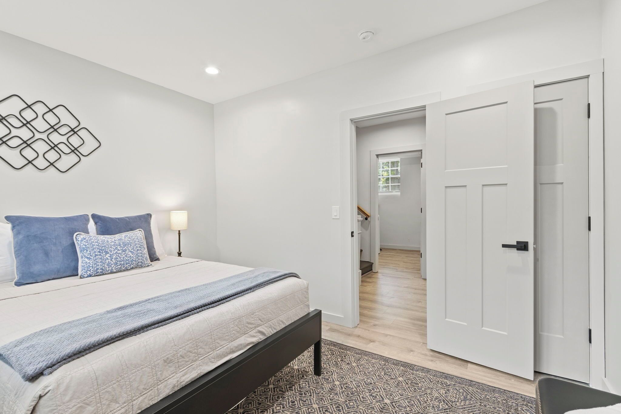 A bedroom with a bed, bedside lamps, a patterned rug, and a hallway leading to another room.