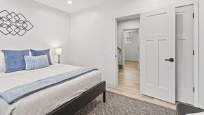 A bedroom with a bed, bedside lamps, a patterned rug, and a hallway leading to another room.