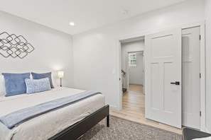 A bedroom with a bed, bedside lamps, a patterned rug, and a hallway leading to another room.