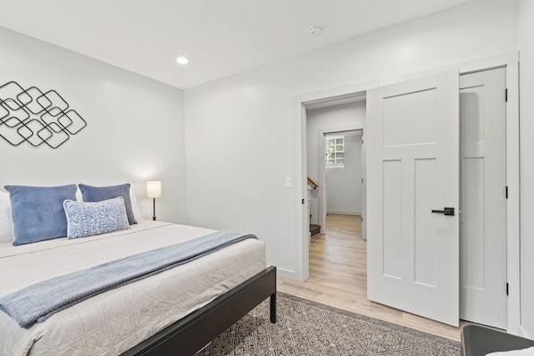 A bedroom with a bed, bedside lamps, a patterned rug, and a hallway leading to another room. - 4BR/3BA Modern GVL Retreat, Fire Pit + Fence (Greenville)