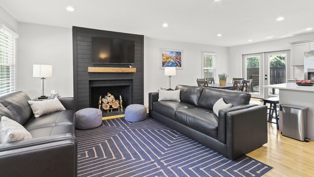 A modern living room with a fireplace, leather sofas, a dining area, and a kitchen.