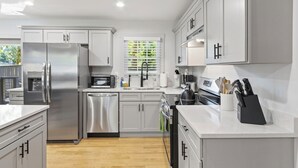 A modern kitchen with stainless steel appliances, white cabinetry, and a wooden floor.
