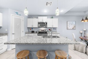 A modern kitchen with white cabinets, a granite countertop, a built-in oven, and a bar area with stools. - Cape Coral Villa with Heated Pool & Dock (Cape Coral)