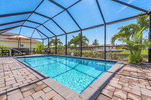 Una piscina exterior coberta amb una superfície d'aigua blava cristal·lina, envoltada d'un pati de maó i vistes a una zona residencial amb palmeres i cases.
