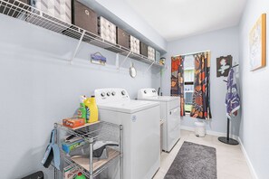 A laundry room with two washing machines, a drying rack, and a shelf with storage boxes. - Villa | Heated Saltwater Pool | Private Gulf Dock (Cape Coral)