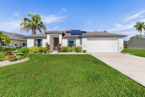 A residential house with a garage, solar panels, and a well-maintained lawn. - Cape Coral Villa with Heated Pool & Dock (Cape Coral)