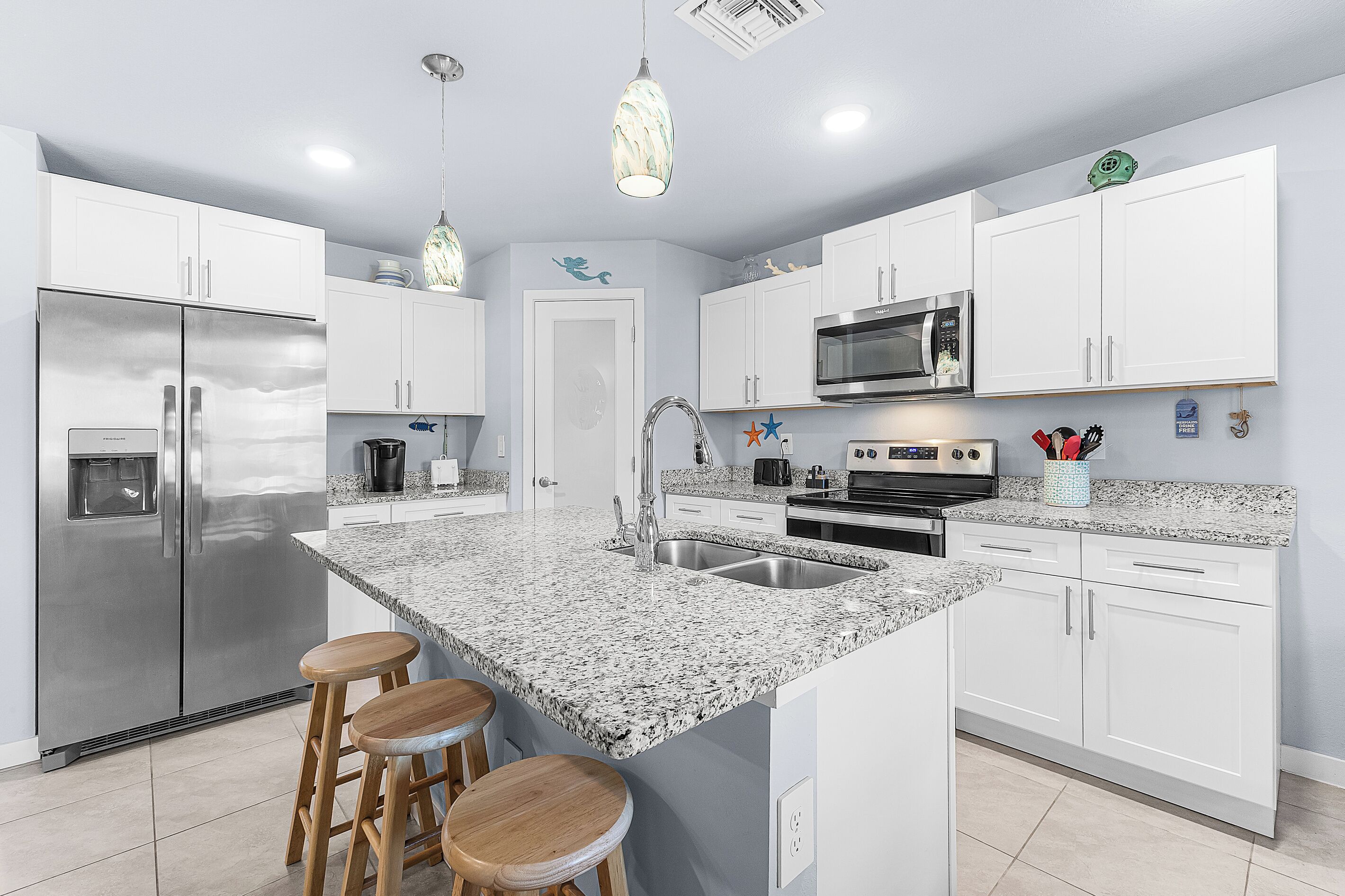 A modern kitchen with white cabinetry, a granite countertop, stainless steel appliances, and a central island with bar stools.