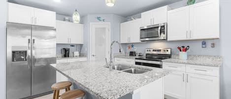 A modern kitchen with white cabinetry, a granite countertop, stainless steel appliances, and a central island with bar stools.