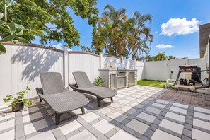 An outdoor patio with two lounge chairs, a barbecue grill, and a stone wall. - Cape Coral Villa with Heated Pool & Dock (Cape Coral)