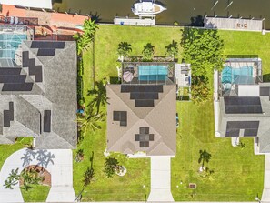 An aerial view of a residential area with multiple buildings, a swimming pool, and solar panels. - Villa | Heated Saltwater Pool | Private Gulf Dock (Cape Coral)