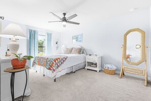 A bedroom with a bed, bedside tables, a nightstand, a mirror, a ceiling fan, and a window with curtains. - Cape Coral Villa with Heated Pool & Dock (Cape Coral)