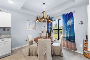A dining area with a chandelier, a table, chairs, and a view of the outdoors through a window. - Villa | Heated Saltwater Pool | Private Gulf Dock (Cape Coral)