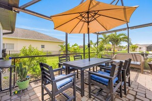An outdoor patio with a table and chairs, a large umbrella, and potted plants. - Villa | Heated Saltwater Pool | Private Gulf Dock (Cape Coral)