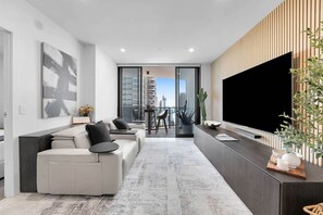 A modern living room with a sofa, a dining area, and a large TV. - Lv 14 Stunning 2 Brm Apt with Skyline Views (Broadbeach)