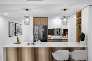 Une cuisine moderne dotée d’un îlot central, d’appareils électroménagers en acier inoxydable, de luminaires suspendus et d’un mur d’accent en bois.