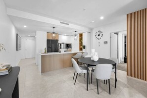 A modern kitchen with a central island, white cabinetry, and a clock on the wall. - Lv 14 Stunning 2 Brm Apt with Skyline Views (Broadbeach)