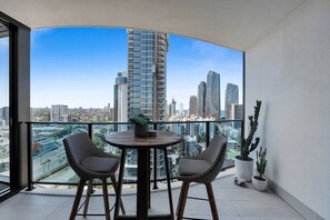 A balcony with a table and chairs, a potted plant, and a view of a cityscape with modern buildings. - Lv 14 Stunning 2 Brm Apt with Skyline Views (Broadbeach)