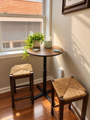 Una habitación pequeña con una mesa redonda, dos sillas de mimbre, una planta en maceta y una caja de pañuelos.
